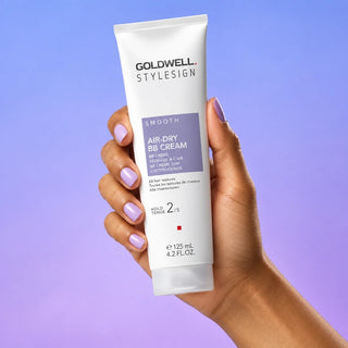 Goldwell StyleSign Air Dry BB Cream held in a woman's hand against a blue and lilac gradient.